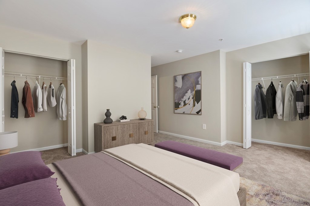 A bedroom with a large bed and a closet with clothes hanging.